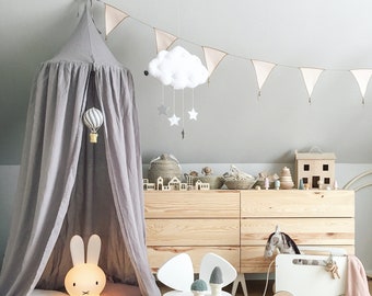 Könnte beinhalten: Ein Kinderzimmer mit einem grauen Baldachin, einer leuchtenden Hasenlampe und einem herzförmigen Kissen in Senfgelb. Ein weißes Wolkenmobile mit Sternen hängt von der Decke. Eine Holzkommode und verschiedene Spielsachen.