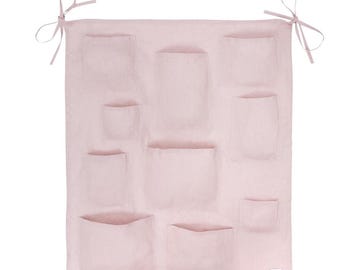 Könnte beinhalten: Ein rosa Wandorganizer aus Leinen mit mehreren Taschen. Der Organizer hat oben und unten zwei Bänder.