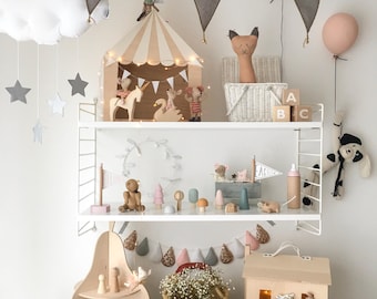 Puede incluir: Una estantería de pared blanca muestra varios juguetes de madera, incluyendo una carpa de circo, figuras de animales, bloques de alfabeto y árboles en miniatura. Debajo, un estante en forma de pera, una cesta tejida y una casa de madera.