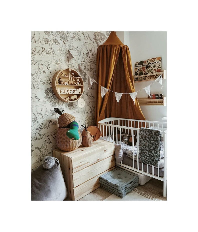 May include: A child's nursery with a white cot, wooden storage, and a round wooden shelf. The room has a mustard-coloured canopy and black and white animal wallpaper. There are soft toys and a grey beanbag. The room is decorated with bunting.