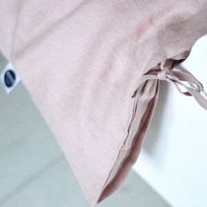 May include: A dusty rose linen duvet cover with ties at the bottom corner. The duvet cover is on a white bed frame.