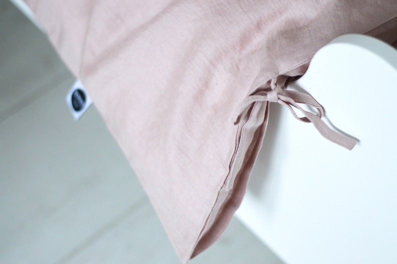 May include: A dusty rose linen duvet cover with ties at the bottom corner. The duvet cover is on a white bed frame.