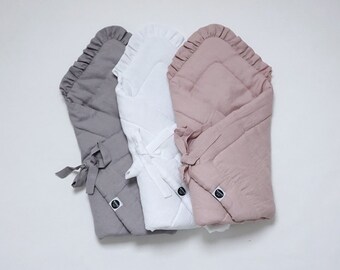 Könnte beinhalten: Drei Baby-Swaddles in verschiedenen Farben: Grau, Weiß und Rosa. Jedes Swaddle hat einen Rüschenrand und ist aus einem weichen, gesteppten Stoff gefertigt. Die Swaddles sind mit Bändern gebunden.