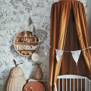 May include: A nursery interior featuring a white cot, a brown canopy, and a wooden shelf with toys and numbers. The room has a wallpaper with a black and white forest design. Wicker pear-shaped baskets and a bear-shaped night light complete the decor.