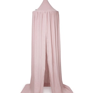 Puede incluir: Un dosel de cama rosa claro con una parte superior c&oacute;nica y tela fluida. La tela cae, creando un espacio suave y cerrado. Una cinta est&aacute; atada en la parte superior para colgar. El dosel est&aacute; hecho de un material ligero.