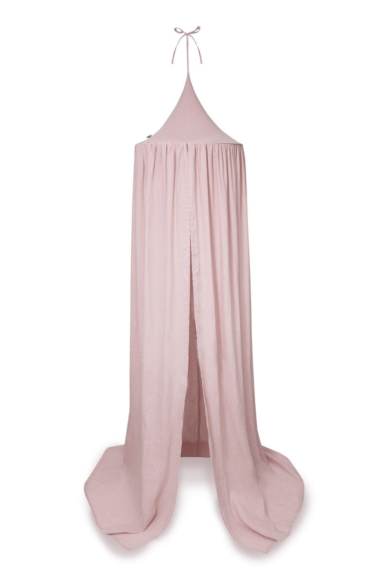 Puede incluir: Un dosel de cama rosa claro con una parte superior c&oacute;nica y tela fluida. La tela cae, creando un espacio suave y cerrado. Una cinta est&aacute; atada en la parte superior para colgar. El dosel est&aacute; hecho de un material ligero.