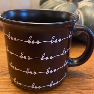 Puede incluir: Taza de cer&aacute;mica negra con un patr&oacute;n blanco de "boo". La taza tiene un asa y es perfecta para Halloween.