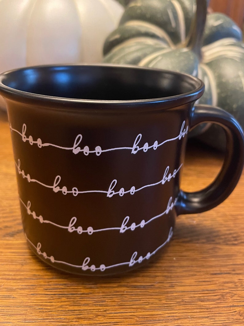 Puede incluir: Taza de cer&aacute;mica negra con un patr&oacute;n blanco de "boo". La taza tiene un asa y es perfecta para Halloween.