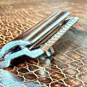 May include: A close-up of a shiny, black metal object with a unique design. The object has a rectangular shape with a grooved edge and a curved, claw-like end. The surface reflects light, creating highlights.