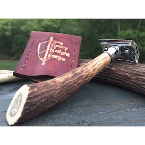 Könnte beinhalten: Ein silberner Sicherheitsrasierer mit einem braunen Hirschhorn-Griff und einem Lederetui mit dem geprägten Text "Avery Knight Forge".