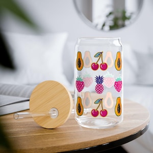 以下が含まれることがあります： 竹製の蓋とストローが付いた、透明なガラス製の缶型グラス。グラスには、パパイヤ、さくらんぼ、イチゴ、パイナップルのカラフルなイラストが描かれています。蓋とストローは竹製です。