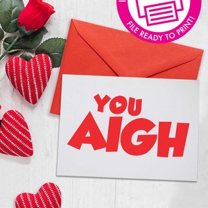 May include: A white card with red text that says "You Aigh" with a small red heart in the "O" of "You". The card is surrounded by red hearts and a red envelope.