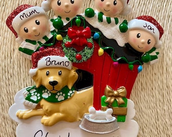 Könnte beinhalten: Ein Weihnachtsbaumschmuck mit einem rot-weißen Haus mit einem grünen Kranz, einem Golden Retriever namens Bruno und vier Familienmitgliedern: Mama, Papa, Lily und Jan. Der Schmuck trägt die Aufschrift "Weihnachten 2021".