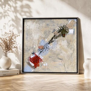 May include: A square abstract painting in a black frame featuring a textured beige background with layered elements including a bold red block, patches of light blue, black ink line work, small white circular patterns, and collage-like paper accents.