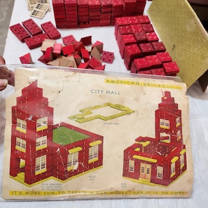 May include: A vintage American Bricks City Hall construction set featuring red plastic building blocks, tan window inserts, and a yellow roof piece. The set includes a printed instruction sheet showing front and rear views of the building model.