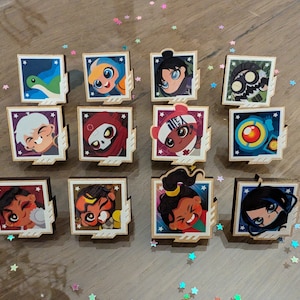 Puede incluir: Doce pines cuadrados de madera con personajes de dibujos animados coloridos. Los personajes son todos diferentes y tienen diferentes expresiones. Los pines están dispuestos en una cuadrícula de cuatro filas y tres columnas.