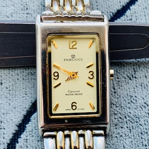 May include: A rectangular Perucci watch with a cream-colored face, gold hands, and gold hour markers. The watch has a silver and gold band. The face reads "PERUCCI", "Expression", and "WATER PROOF". The watch is marked "JAPAN" and "23-1549".