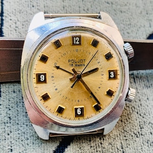 Puede incluir: Un reloj de pulsera vintage Poljot 18 jewels con esfera dorada y caja plateada. La esfera muestra marcadores de hora rectangulares negros y los n&uacute;meros 3, 6, 9 y 12. El reloj est&aacute; sujeto a una correa de cuero marr&oacute;n.