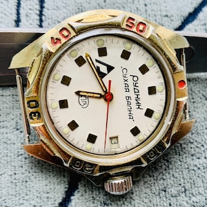 May include: Vintage wristwatch with a white face, black and red numerals, and gold-toned bezel. The watch features a date window at the 3 o'clock position and a red second hand. The watch case is approximately 40mm in diameter.
