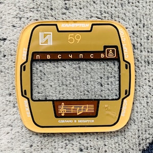 May include: A vintage gold-colored radio faceplate with the text "KAMERTON" at the top. The faceplate has a rectangular window, a musical note graphic, and the number "59". The text "Made in Belarus" is also visible.