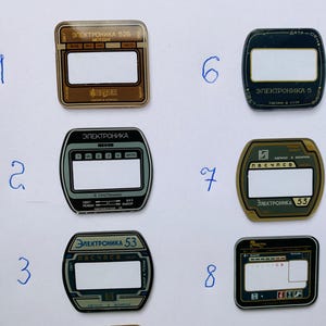 May include: A collection of eight vintage electronic device faceplates. The faceplates feature rectangular and rounded designs with text in Cyrillic script. Colors include brown, black, and gray, with white and gold accents. The faceplates are likely from Soviet-era electronics.