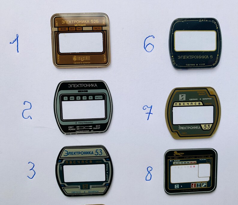 May include: A collection of eight vintage electronic device faceplates. The faceplates feature rectangular and rounded designs with text in Cyrillic script. Colors include brown, black, and gray, with white and gold accents. The faceplates are likely from Soviet-era electronics.