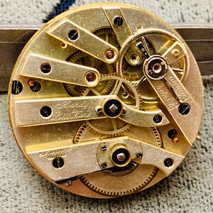 K&ouml;nnte beinhalten: Nahaufnahme eines antiken Uhrwerks mit komplexen Zahnr&auml;dern und Mechanismen. Die goldfarbenen Komponenten sind kreisf&ouml;rmig angeordnet, mit den Inschriften "Hardy Petit Mars" und "D. Jacotte Travere".
