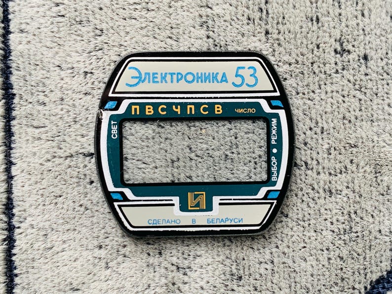 May include: A rectangular, black and white electronic device component with the text "Электроника 53" in blue. The component has a teal and white border and includes Cyrillic text and the words "Made in Belarus".