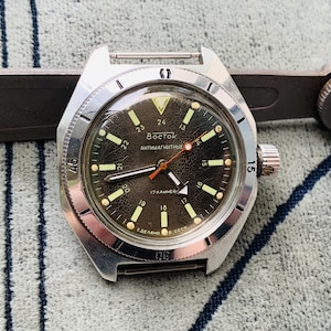 Puede incluir: Un reloj de pulsera plateado con una esfera negra y marcas blancas. La esfera del reloj tiene el texto "Восток АНТИМАГНИТНЫЕ 17 КАМНЕЙ СДЕЛАНО В СССР" impreso en él.