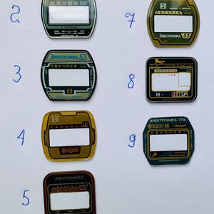 May include: A collection of nine vintage electronic device faceplates. Each plate features a rectangular display area, with text in Cyrillic script and various colors, including green, gold, and black. The faceplates are numbered 2 through 9.