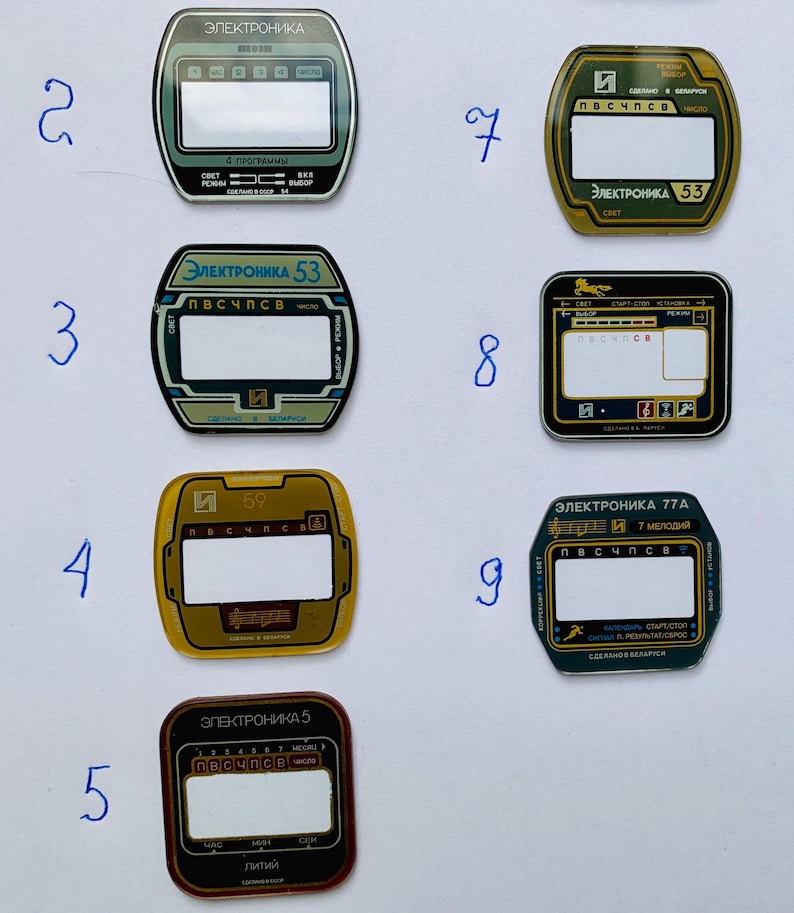 May include: A collection of nine vintage electronic device faceplates. Each plate features a rectangular display area, with text in Cyrillic script and various colors, including green, gold, and black. The faceplates are numbered 2 through 9.