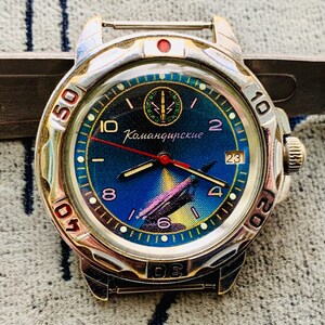 Puede incluir: Un reloj de pulsera plateado con esfera azul y amarilla. La esfera del reloj presenta el texto "Командирские" y un gráfico de un avión. El reloj tiene un segundero rojo y una indicación de fecha a las 3 en punto.