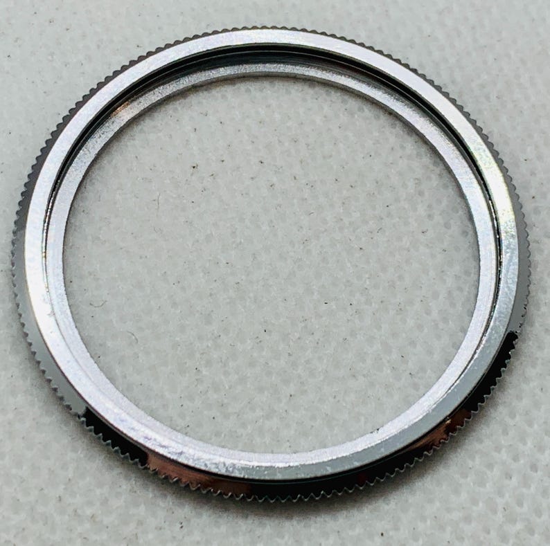 Op de afbeelding: Een zilverkleurige horloge bezel met een gladde, ronde rand.