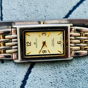 May include: A rectangular Perucci watch with a gold-tone face and hands, featuring gold hour markers and the numbers 12, 3, 6, and 9. The watch has a silver and gold-tone link band. The watch face reads "Expression Water Proof" and "Japan".