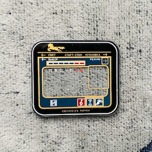 May include: A black and gold rectangular control panel with a horse silhouette and Cyrillic text. The panel has a blue and gold border, with icons and text in white and red. The panel is on a gray, textured surface.