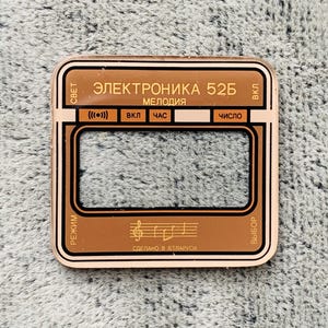 May include: A copper-colored rectangular device with black and gold accents. The text "ЭЛЕКТРОНИКА 52Б" and other Cyrillic text are visible. The device has a rectangular display area and several buttons. The words "СДЕЛАНО В БЕЛАРУСИ" are also visible.