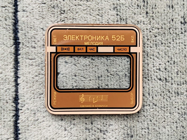 May include: A copper-colored rectangular device with black and gold accents. The text "ЭЛЕКТРОНИКА 52Б" and other Cyrillic text are visible. The device has a rectangular display area and several buttons. The words "СДЕЛАНО В БЕЛАРУСИ" are also visible.