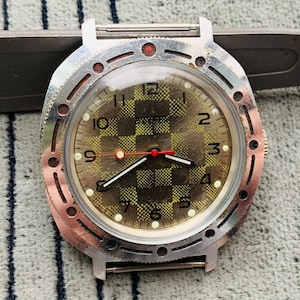 May include: A vintage silver wristwatch with a chequered face and red hands. The watch has a black bezel with white markings and a silver band.
