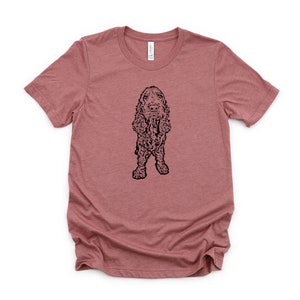 May include: A heather pink t-shirt with a black line drawing of a Cocker Spaniel dog.