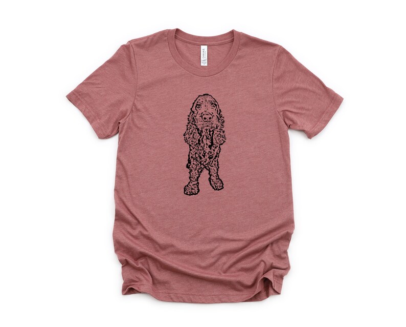 May include: A heather pink t-shirt with a black line drawing of a Cocker Spaniel dog.