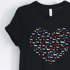 May include: Black t-shirt with a red, white, and blue heart design made up of dachshund silhouettes. The heart is surrounded by small red, white, and blue hearts and paw prints.
