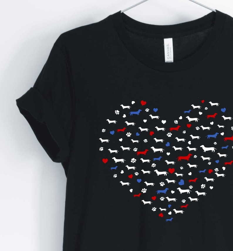 May include: Black t-shirt with a red, white, and blue heart design made up of dachshund silhouettes. The heart is surrounded by small red, white, and blue hearts and paw prints.