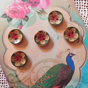 May include: Six decorative wooden buttons with a floral design in red, green, and beige. The buttons are arranged on a card featuring a peacock illustration and pink roses. The buttons are approximately 1 inch in diameter.