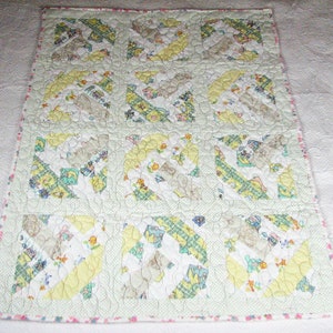 May include: A handmade baby quilt featuring a patchwork design with squares of white, yellow, and green fabric. The quilt has a light green border with a pink floral trim. The squares are patterned with cartoon animals and toys.