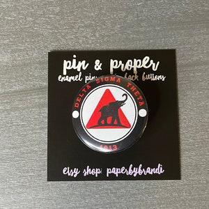 May include: A black and white enamel pin with a red triangle and a black elephant silhouette. The pin says "Delta Sigma Theta 1913" around the edge.