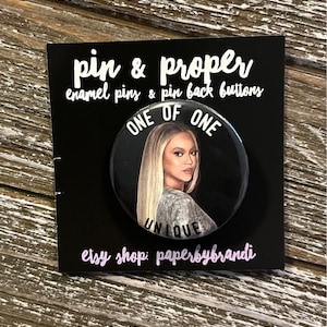 May include: A black pin with a portrait of a woman with blonde hair, the text "ONE OF ONE" and "UNIQUE". The pin is on a black card with the text "pin & proper" and "etsy shop: paperbybrandi".