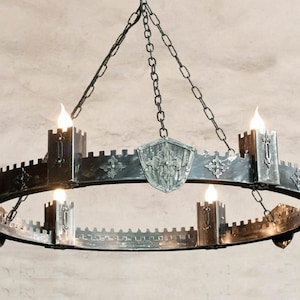 May include: A black metal chandelier with a circular design and six candle holders. The chandelier is suspended from a chain and has a shield-shaped design in the center.