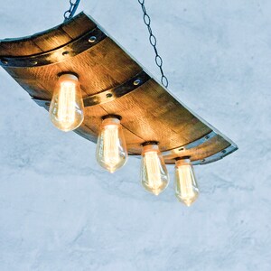 May include: A rustic wooden chandelier with four exposed light bulbs. The chandelier is made from a repurposed wine barrel stave and has a metal chain hanging from the ceiling.