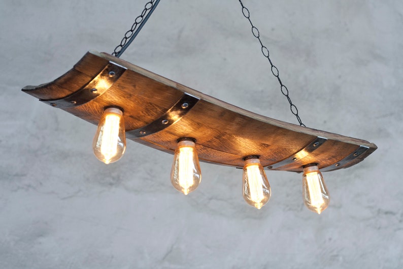 May include: A rustic wooden chandelier with four Edison bulbs hanging from a black chain. The chandelier is made from a reclaimed wine barrel stave and has metal accents.