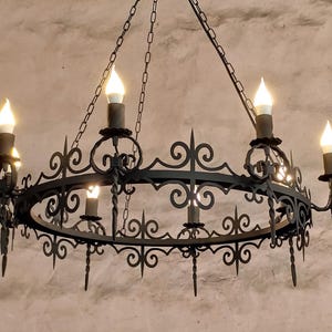 Puede incluir: Una lámpara de araña de hierro forjado negro con un marco circular y seis bombillas de estilo candelabro.